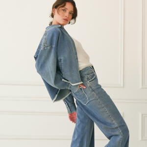 Imagebild: Model steht vor Stuckwand und trägt ÉLÉGANCE DENIM Jeans und Jeansjacke.