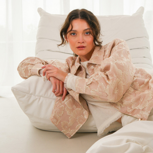 Imagebild: Model sitzt auf Sessel und trägt JACQUARD ROSÉ Jacke.