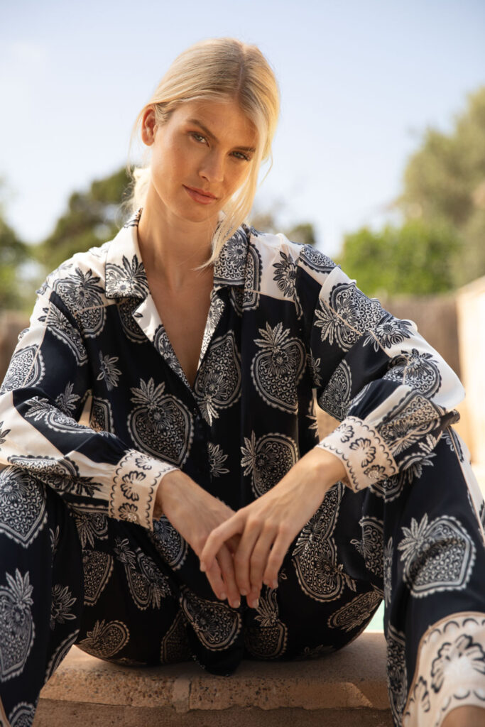 Imagebild: Model sitzt vor Finka und trägt STRAWBERRY Seidenbluse und Seidenhose.