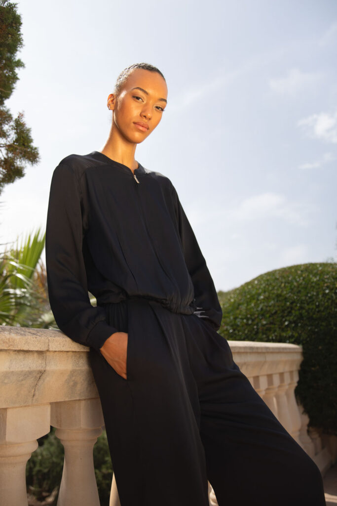 Imagebild: Model steht vor Finka und trägt SOLID SILK Seidenblouson und Seidenhose in dunkelblau.