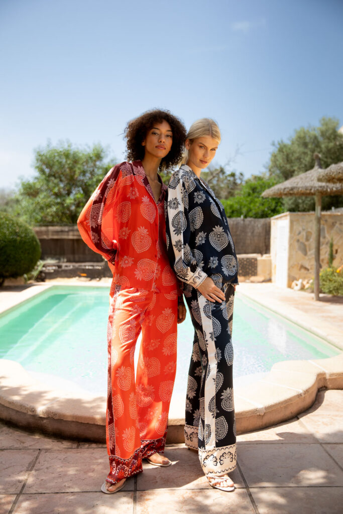 Imagebild: Models stehen vor Pool und tragen STRAWBERRY Bluse und Hose in rot und blau.