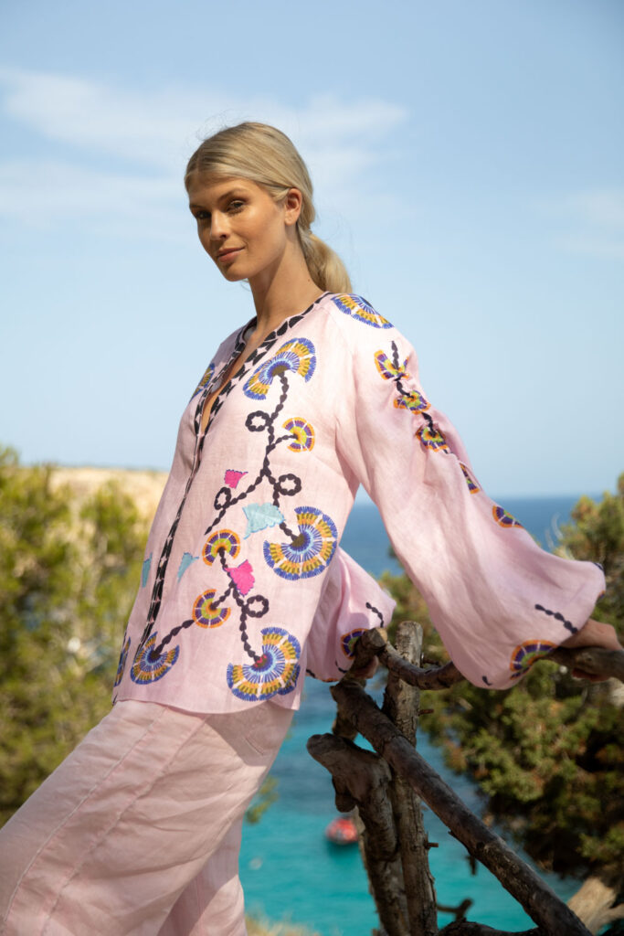 Imagebild: Model steht vor einer Meeresbucht und trägt das FOLDED FLOWERS Leinenbluse.