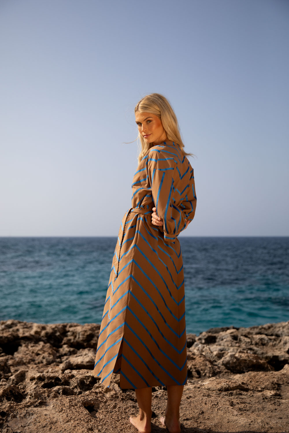 Imagebild: Model steht auf Küstenklippen vor dem Meer und trägt das ROYAL STRIPE Baumwollkleid.
