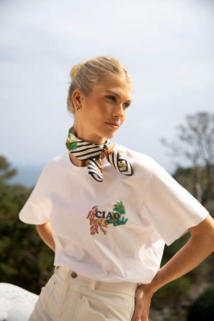 Imagebild: Model auf Balkon mit Meerblick. Sie trägt das CAMOU T-Shirt und das CAMOU Seidentuch.
