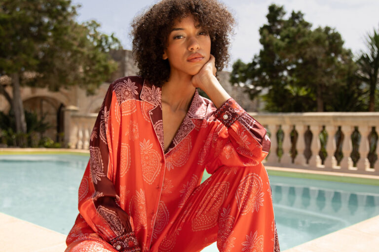Imagebild: Model sitzt vor Pool und trägt STRAWBERRY Seidenbluse und Seidenhose.